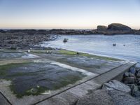 a fire hydrant next to the ocean with rocks and water surrounding it with boats on the water