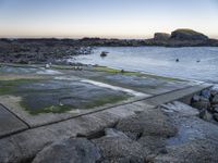 a fire hydrant next to the ocean with rocks and water surrounding it with boats on the water