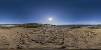 a panoramic photo of a dirt path leading to the beach under a blue sky with a sun behind it