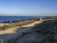 the dirt road leading to the shore is empty and sandy on the other side is an ocean