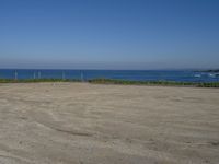 an open field with some very empty beaches and a blue water in the background on a clear day