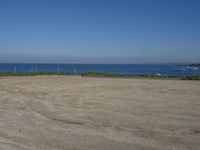 an open field with some very empty beaches and a blue water in the background on a clear day