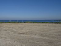 an open field with some very empty beaches and a blue water in the background on a clear day