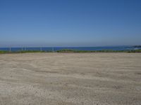 an open field with some very empty beaches and a blue water in the background on a clear day