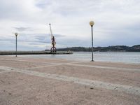 a view looking out at the water and cranes on a pier with grey cloudy sky above