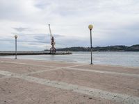 a view looking out at the water and cranes on a pier with grey cloudy sky above