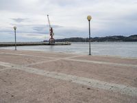 a view looking out at the water and cranes on a pier with grey cloudy sky above