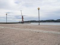 a view looking out at the water and cranes on a pier with grey cloudy sky above