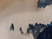 an aerial view of people riding horses through the snow near mountains and sand dunes of the desert