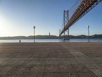 a large bridge is crossing the water at sunset time as seen from the sidewalk near the water