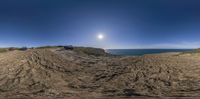 two vehicles driving through mud in the sand by the ocean under a sun haloe