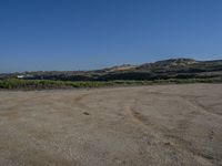 a dirt field with an over head view of hills in the distance and a blue sky above