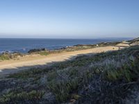 a long empty road and dirt path near the ocean on a clear day with a few people sitting on it