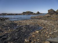 rocky shore on an island in the sea with several rocks in the water and a small boat out on the water