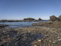 rocky shore on an island in the sea with several rocks in the water and a small boat out on the water