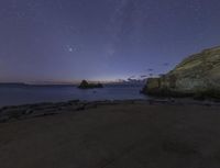 a rocky coast at night with the stars in the sky overhead and a few small rocks on the beach