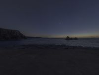 an ocean with rocks under the moonlight light and a crescenty sky in the background