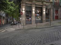 a cobble stone street at night, lined with parked cars and trees along the sidewalk