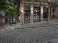 a cobble stone street at night, lined with parked cars and trees along the sidewalk