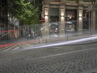 a cobble stone street at night, lined with parked cars and trees along the sidewalk