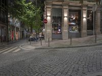 a cobble stone street at night, lined with parked cars and trees along the sidewalk