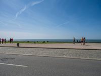 the tourists are walking on the sidewalk near the water and a grassy area next to the ocean