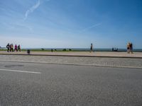 the tourists are walking on the sidewalk near the water and a grassy area next to the ocean