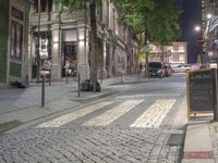 an empty city street at night with people walking by it and sign on the sidewalk