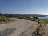 a winding road leads to an island with mountains in the distance and a body of water with hills on either side