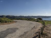 a winding road leads to an island with mountains in the distance and a body of water with hills on either side