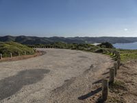 a winding road leads to an island with mountains in the distance and a body of water with hills on either side