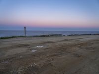 a sandy road on the beach near the ocean at sunset or dawn with a clock post and water puddles