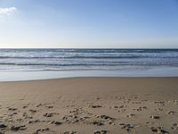 footprints on the beach with waves rolling in in the distance and sun shining down onto the ocean