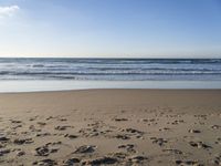 footprints on the beach with waves rolling in in the distance and sun shining down onto the ocean