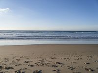 footprints on the beach with waves rolling in in the distance and sun shining down onto the ocean