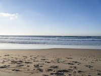 footprints on the beach with waves rolling in in the distance and sun shining down onto the ocean