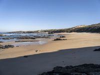 large rocks in foreground near water, at edge of rocky beach, with grassy hill and beached coastline