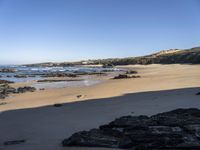 large rocks in foreground near water, at edge of rocky beach, with grassy hill and beached coastline