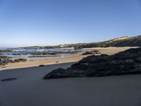 large rocks in foreground near water, at edge of rocky beach, with grassy hill and beached coastline