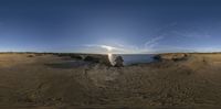 the sun is shining over the ocean on the beach rocks and sand dunes are in the foreground