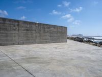 a large concrete wall on a beach by the ocean with a boat nearby in the water
