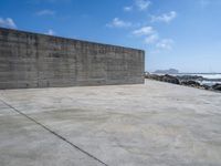 a large concrete wall on a beach by the ocean with a boat nearby in the water