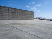 a large concrete wall on a beach by the ocean with a boat nearby in the water