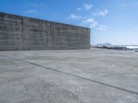 a large concrete wall on a beach by the ocean with a boat nearby in the water