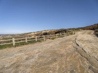 a dirt road with fence around it leading to the ocean, and mountains in the background