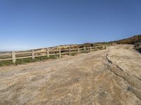 a dirt road with fence around it leading to the ocean, and mountains in the background