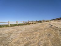 a dirt road with fence around it leading to the ocean, and mountains in the background