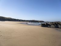 a sandy beach with steps leading up to a hill near an ocean and a hotel