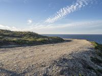 an open dirt road along a grassy hill near the ocean shore line of a coastal beach