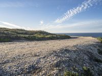 an open dirt road along a grassy hill near the ocean shore line of a coastal beach